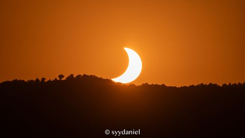 The eclipsed sun setting over the hills.